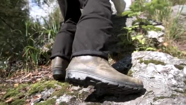 Cerrar para senderismo botas de goma en acción en un camino rocoso. Hombre haciendo pasos para subir una montaña en un día soleado
. - Metraje, vídeo