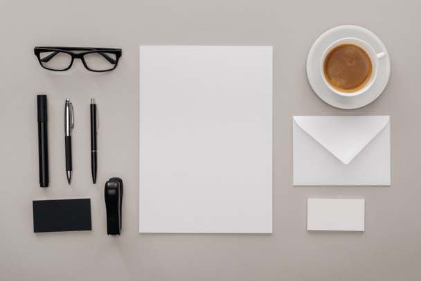 flat lay with black glasses, stationery and white empty cards at workplace with cup of coffee on grey background - Photo, Image