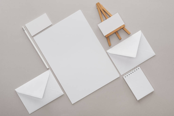 flat lay with white empty papers and letters with toy easel at workplace on grey background - Foto, Bild
