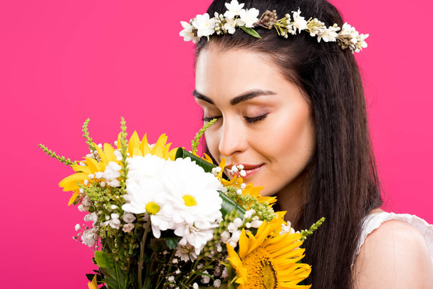 beautiful young brunette woman in floral wreath smelling flower bouquet isolated on pink - Φωτογραφία, εικόνα