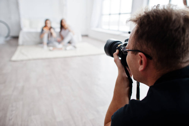 Man photographer shooting on studio two girls. Professional photographer on work. - Fotó, kép