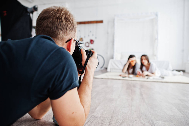 Man photographer shooting on studio twins girls who are eating pizza. Professional photographer on work. - Foto, Imagen