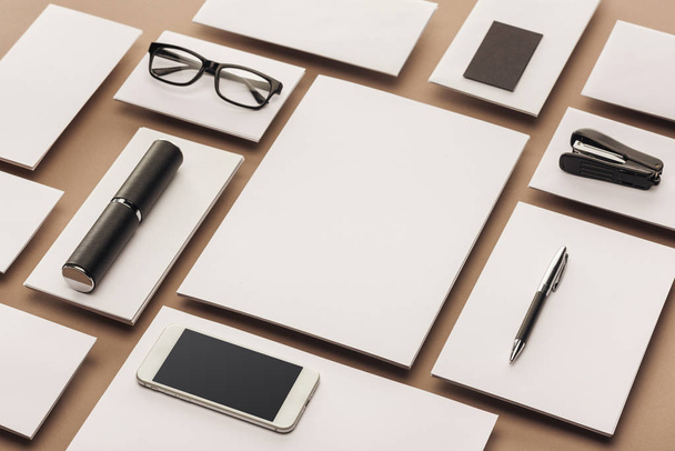 Empty sheets of paper, case, glasses, smartphone, pen and stapler on beige background - Foto, Bild