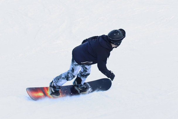 Lumilautailija ratsastaa lumilaudalla alas lumen peitossa rinteessä hiihtokeskuksessa. Talviurheilua. Freestyle ja pujottelu laskeutuminen. Laitteet äärimmäiseen kylmyyteen. Aktiivisuus terveyteen kylmässä. Nuorten harrastus
. - Valokuva, kuva