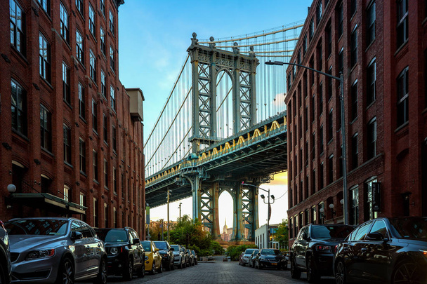 Pont de Manhattan vu d'une ruelle étroite entourée de deux bâtiments en briques par une journée ensoleillée en été
  - Photo, image