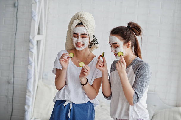 Deux jumelles en pyjama avec masque facial et tranches de concombre
. - Photo, image