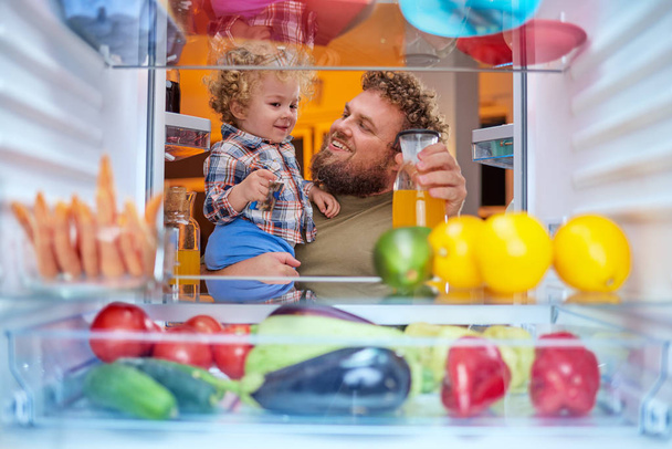 父と息子の夜遅くの冷蔵庫から食べ物を取ってします。冷蔵庫の中から撮影した写真. - 写真・画像