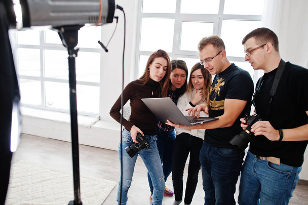 Photographer explaining about the shot to his team in the studio and looking on laptop. Talking to his assistants holding a camera during a photo shoot. Teamwork and brainstorm. - Foto, immagini