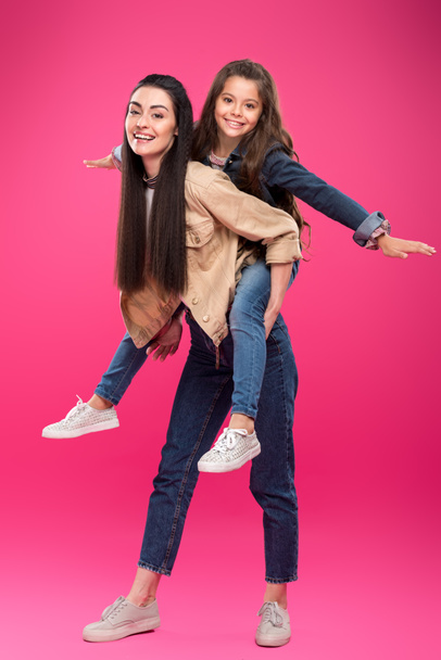 full length view of beautiful happy mother and daughter piggybacking and smiling at camera isolated on pink - Foto, immagini