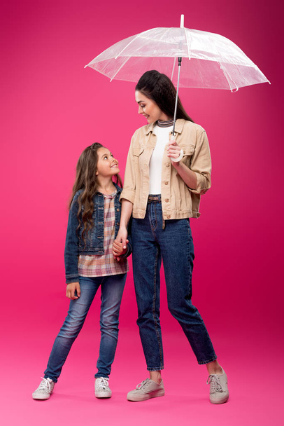 happy daughter and mother with umbrella holding hands and smiling each other on pink - Foto, Bild
