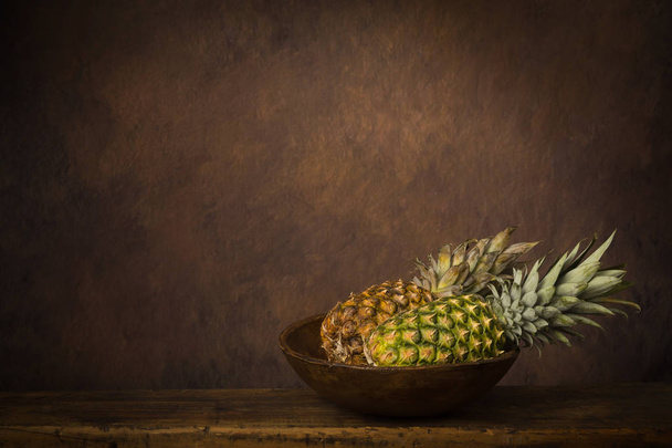 Sötét csendélet friss ananásszal egy antik fa asztalon. - Fotó, kép