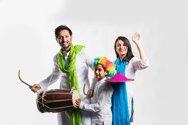 Çocuklu Hintli genç bir çift Holi festivalini kutluyor. Dans eder, davul çalar ve tabak dolusu renk taşır. - Fotoğraf, Görsel
