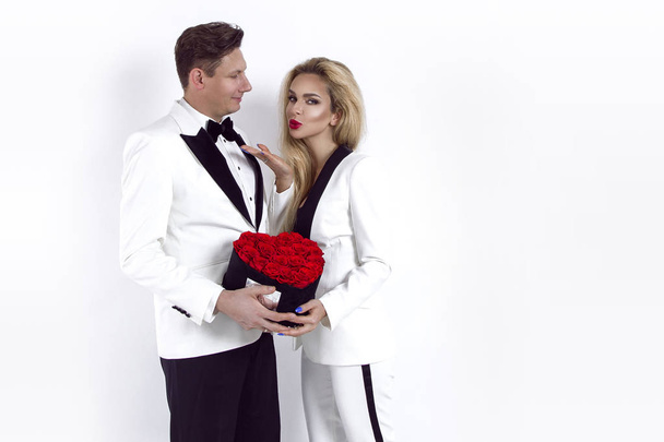 Feliz hermosa pareja posando sobre fondo blanco y sosteniendo caja de flores con corazón rojo. San Valentín, boda - Imagen
 - Foto, Imagen