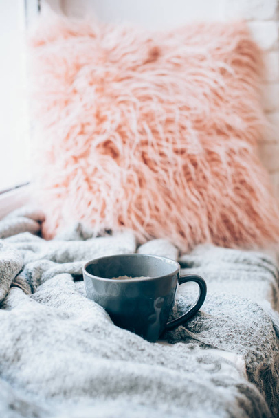 Cup of coffee, knitted blanket and fluffy pillow on cozy windowsill - Photo, Image