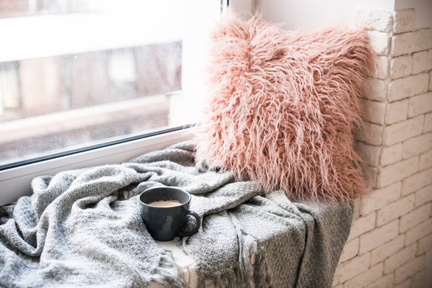 Xícara de café, cobertor de malha e travesseiro fofo no peitoril da janela aconchegante
 - Foto, Imagem