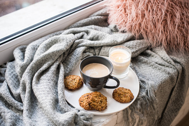 Desayuno estilo escandinavo, taza de café y galletas en el acogedor alféizar de la ventana con manta caliente y almohada
 - Foto, Imagen
