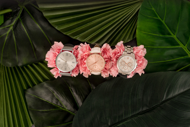 top view of wristwatches lying on blooming pink flowers near green leaves - Photo, Image