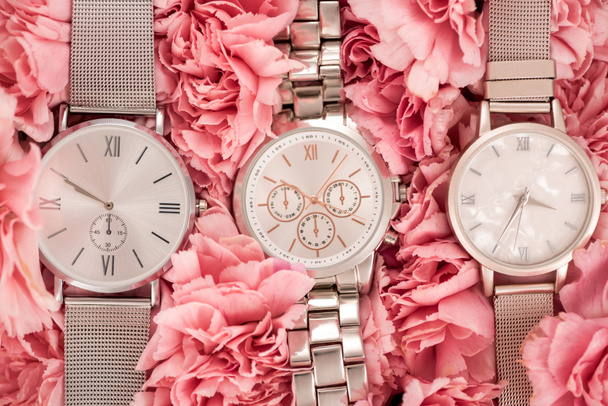 top view of wristwatches lying on blooming pink carnations  - Photo, Image