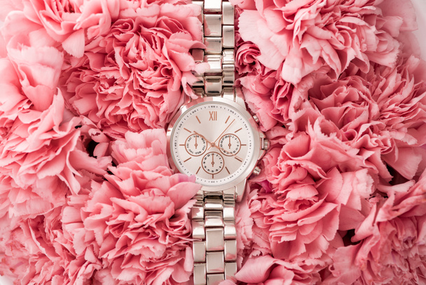 top view of elegant wristwatch lying on blooming flowers - Foto, Imagen