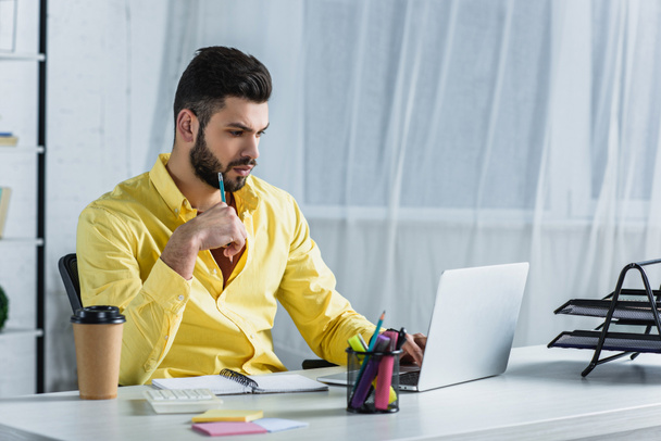 Сфокусированный бородатый бизнесмен смотрит на экран ноутбука и держит карандаш
   - Фото, изображение