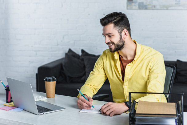 Empresário sorrindo usando laptop e escrevendo em notebook
 - Foto, Imagem