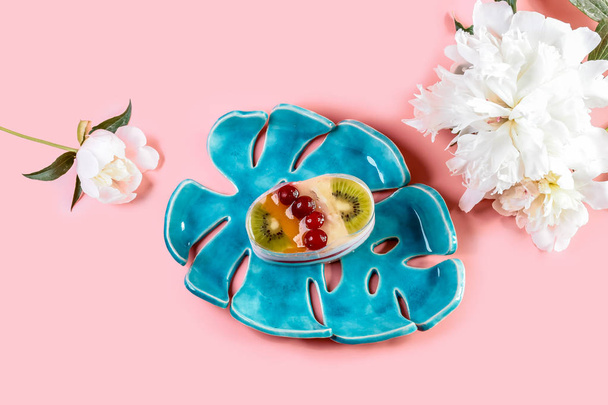 Fruit dessert cake with spring flowers of the pion on a blue ceramic plate, isolated on pink background. - Foto, Imagen