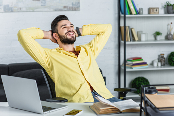 Smiling bearded businessman in yellow shirt with crossed arms looking up at workplace - Foto, imagen