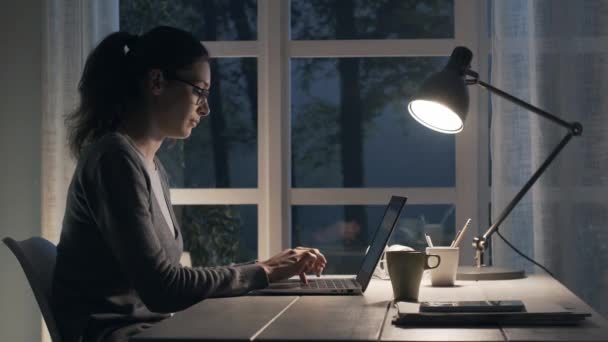 Unavená žena sedí na stole doma a práce pozdě v noci se její laptop, je ospalý a koncept s a bolest hlavy, stres a termíny - Záběry, video