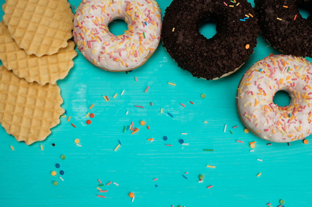 four donuts, chocolate and with white cream and wafers lie in a semicircle on a wooden turquoise backgroun. Cropped image - Foto, Imagen
