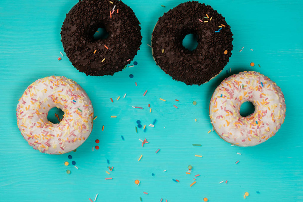 four donuts, chocolate and with white cream, lie in a semicircle on a wooden turquoise background - Foto, Imagen