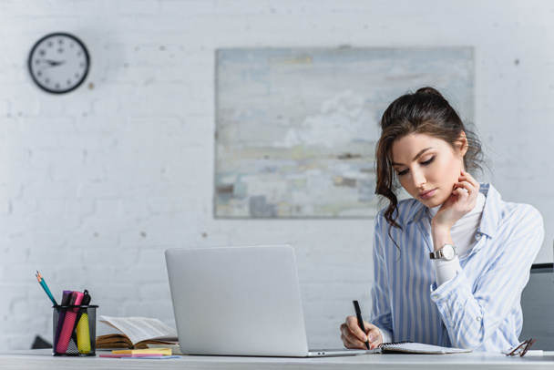 Focused attractive businesswoman writing in notebook at workplace - Photo, Image