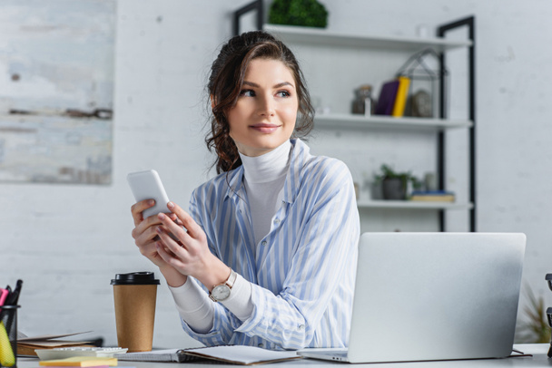 Femme d'affaires attrayante tenant smartphone et regardant loin au bureau
 - Photo, image