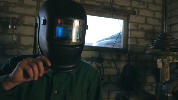 Mechanic opens mask after finishing his work. Tired man looks into camera. Guy with beard working in his garage or workshop. Male worker wears protective mask for his safety. Slow motion Dolly shot - Footage, Video