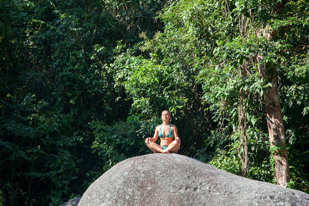 Mujer joven meditando sobre una roca en el fondo de un bosque tropical
. - Foto, Imagen