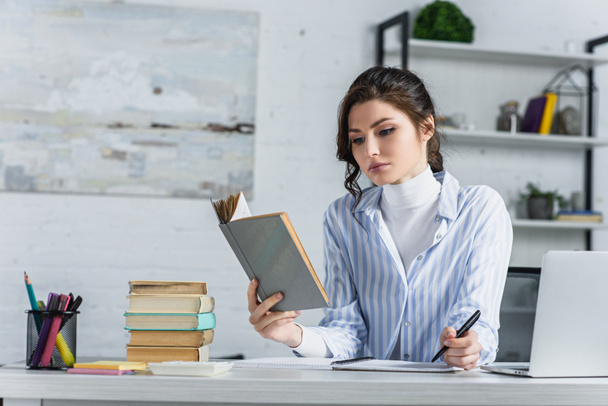 donna triste che studia con il libro mentre tiene la penna in mano nell'ufficio moderno
  - Foto, immagini