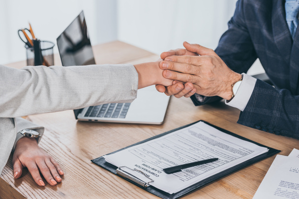 cropped view of businessman holding woman hand over table in office, compensation concept - Photo, Image