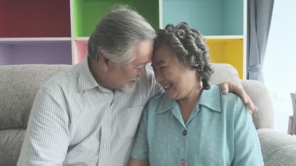 Senior couple sitting and hugging each other in living room. Retired old Asian male and female, talking and holding each other, happy smile. Senior lifestyle concept. - Filmagem, Vídeo