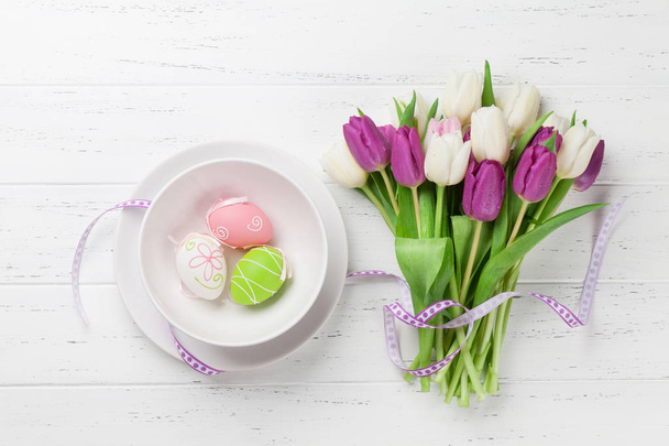 Cartão de Páscoa com flores de tulipa buquê e ovos de Páscoa. Vista superior sobre mesa de madeira branca
 - Foto, Imagem