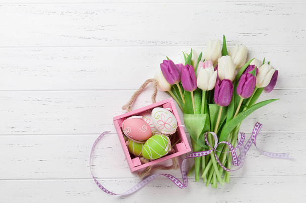 Easter greeting card with tulip flowers bouquet and easter eggs. Top view over white wooden table with space for your greetings - 写真・画像