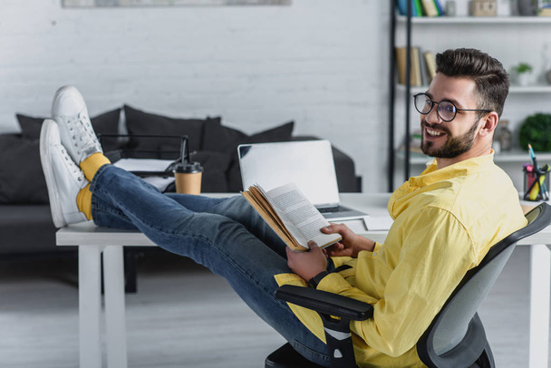 selective focus of cheerful man studying with legs on table in modern office - Фото, зображення