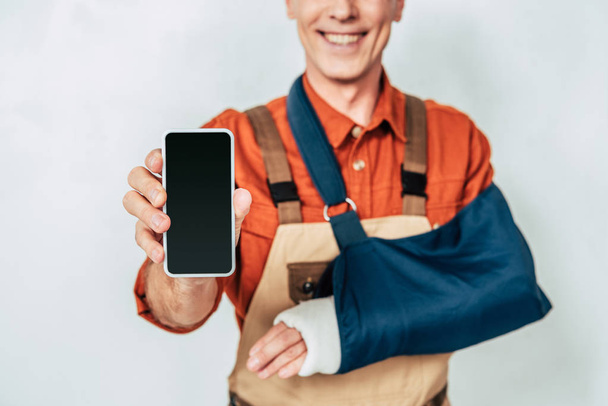 обрезанный вид ремонтника с повязкой на руке показывает пустой смартфон с чистым экраном на белом фоне
 - Фото, изображение