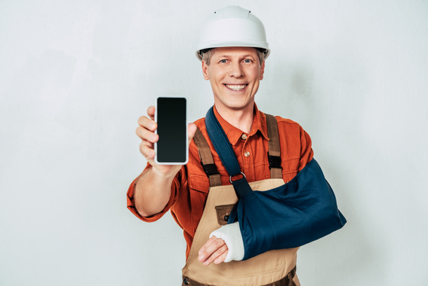 reparador con vendaje de brazo que muestra el teléfono inteligente en el fondo blanco
 - Foto, Imagen