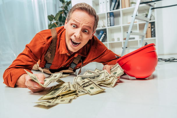 reparador sorprendido en uniforme acostado en el piso cerca del dinero en la oficina
 - Foto, imagen