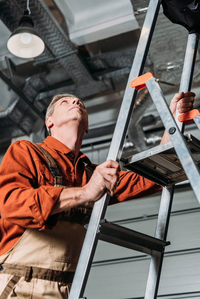 repairman in orange uniform standing on ladder in garage - Fotó, kép