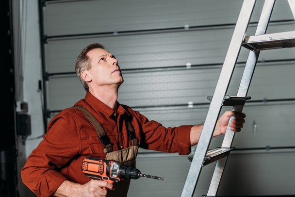 repairman climbing with screwdriver on ladder in garage - Photo, Image