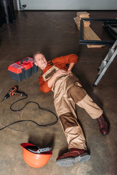 repairman lying on floor near ladder and holding on side in garage - Foto, afbeelding