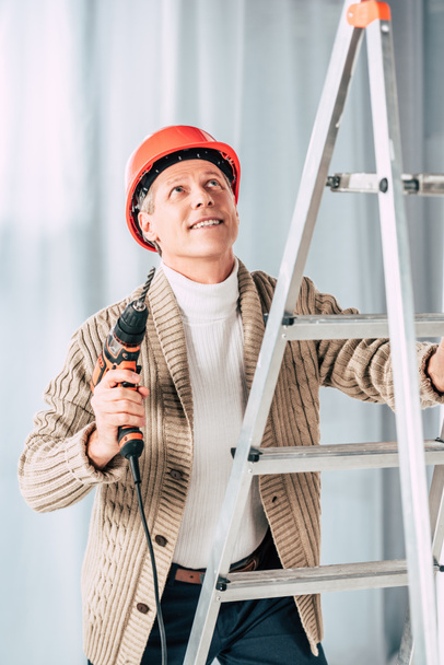 middle aged man in beige cardigan climbing with screwdriver on ladder at home - Foto, immagini
