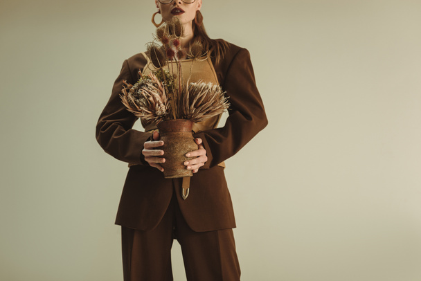 vue recadrée d'une femme élégante tenant une cruche en argile avec des fleurs sèches isolées sur beige
 - Photo, image