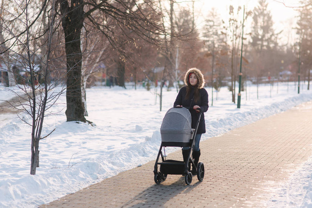 Прекрасная мать, гуляющая в парке со своим малышом в Столлере. Женщина в синем жакете с капюшоном и джинсами. Теплые сапоги
 - Фото, изображение
