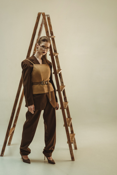 attractive woman in vintage style posing near wooden ladder on beige - Photo, Image
